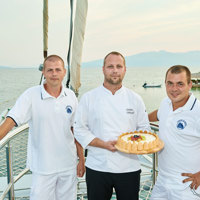 chef and crew standing at ship's nose holding a cake